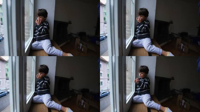 孩子坐在家里的窗户边抠鼻子，从公寓向外看，无聊的小男孩被锁在室内