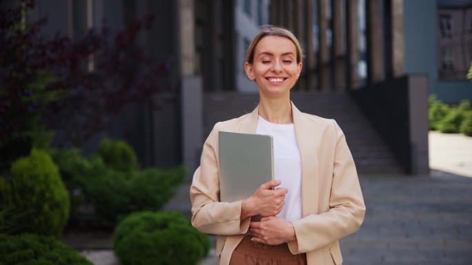 自信迷人的女商人的肖像，女人看着镜头微笑着拿着笔记本电脑，风吹着头发，骄傲的企业家在外面享受成功的创