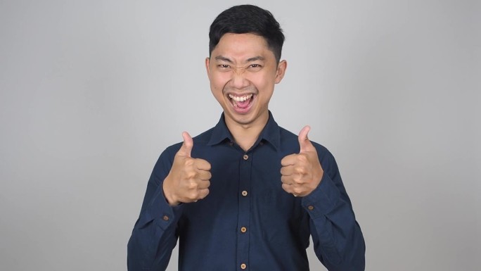 年轻的亚洲男子欢快的微笑显示双拇指为成功白色背景