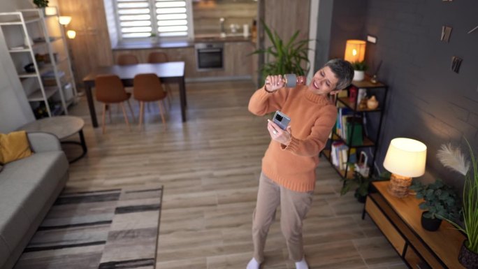 一个成熟的女人一边在客厅唱卡拉ok一边用手机拍视频