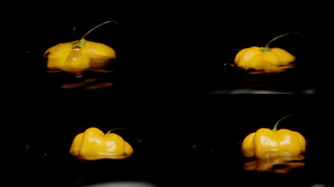 一个黄色的哈瓦那辣椒落入水中，背景是黑色的慢动作特写。