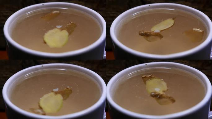 桌上有一大杯茶。POV:一个人看着桌上的热姜蜂蜜茶。姜片在一杯茶里打转。蜂蜜茶。姜茶。一大杯茶，特写