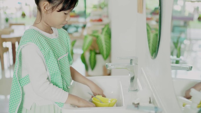 小学混合女孩在蒙台梭利教育学校洗碗，实践生活技能活动
