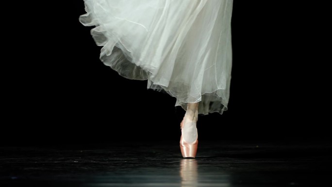 优雅的芭蕾舞者穿着白色的芭蕾舞裙，在Pointe鞋中跳芭蕾舞和平衡，双腿的视角，黑暗的背景，小心的步