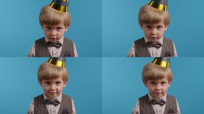 微笑的小寿星戴着圆锥形的帽子在蓝色的墙壁背景。快乐的情感孩子。惊奇的眼神，快乐的童年