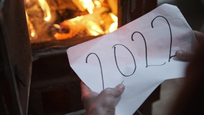 一名男子将一张写着2022字样的纸揉成一团，扔进了燃烧的火炉。燃烧木头的炉子里红色和黄色的火焰。石炉