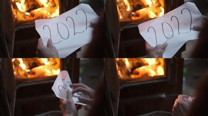 一名男子将一张写着2022字样的纸揉成一团，扔进了燃烧的火炉。燃烧木头的炉子里红色和黄色的火焰。石炉