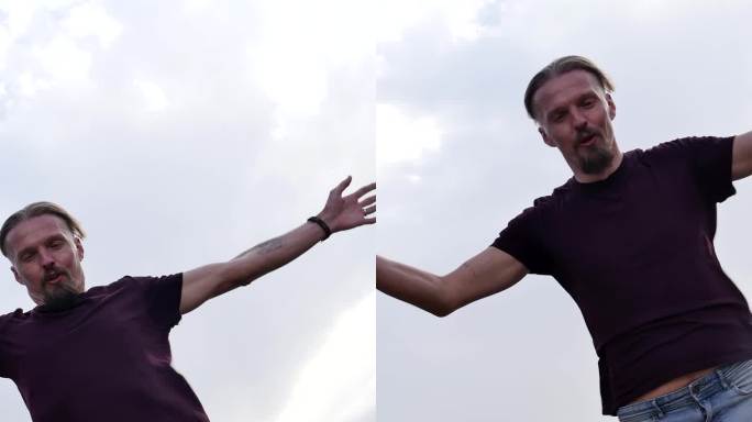 垂直全长肖像，一个年轻的长发男子在山上冥想，在强风中，他的手臂分开，享受冥想的苦修板。垂直视频