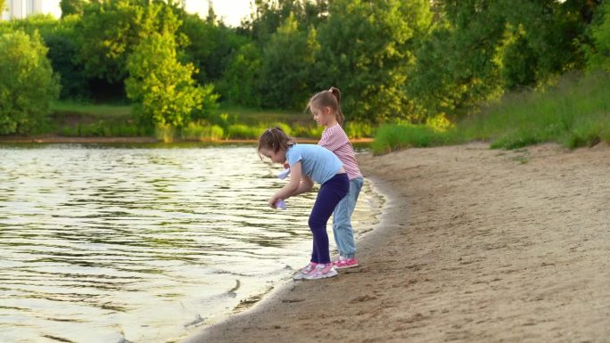 夕阳下，以夏日公园为背景，女孩们在河上玩纸船