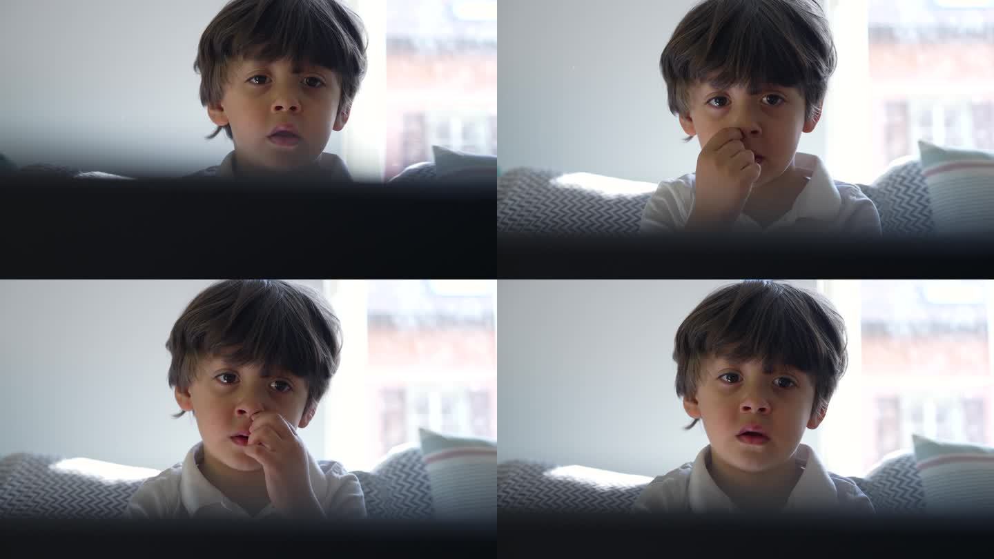 小男孩盯着电视屏幕挖鼻孔的特写，孩子沉浸在家里的娱乐中