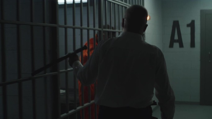 拿着警棍的狱卒看着监狱里的罪犯