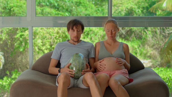 在这个幽默的慢镜头视频中，一位孕妇开玩笑地把一个西瓜拴在她男人的肚子上，创造了一个轻松的模拟怀孕的体