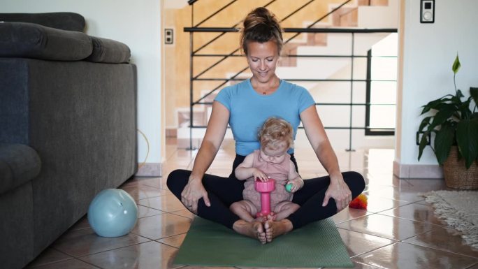 一名妇女和婴儿坐在客厅的瑜伽垫上