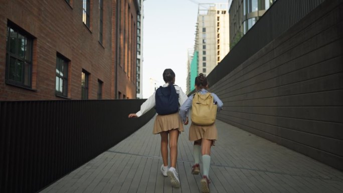 两个女学生上学的后视图。同学们背着书包在学校大楼前。