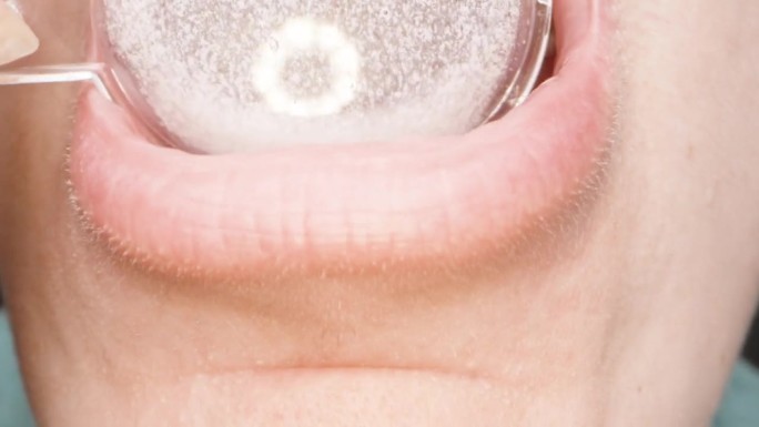 一个女人用一个量匙喝着，白色的止咳糖浆，在她的嘴里。