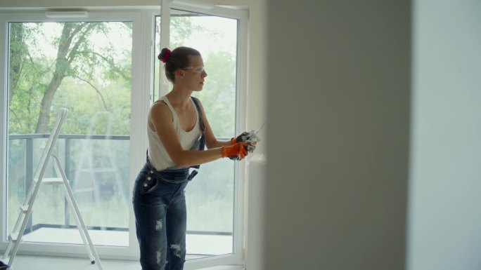 年轻女子用油漆滚筒刷着她梦想中的房子墙壁。穿戴防护服和护目镜