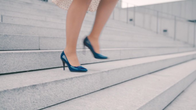 一个美丽的商业女性的特写，她的腿穿着颜色多变的高跟鞋走下楼梯