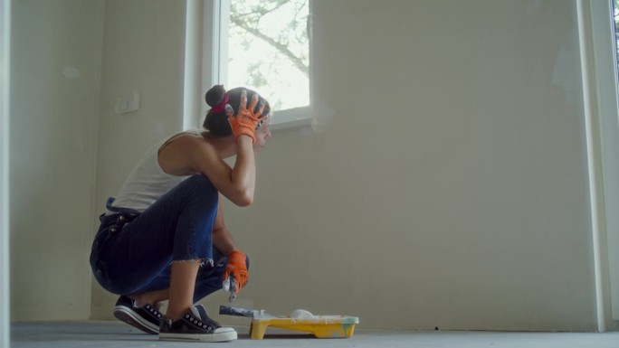 年轻女子正在粉刷她梦想中的房子墙壁。休息一下