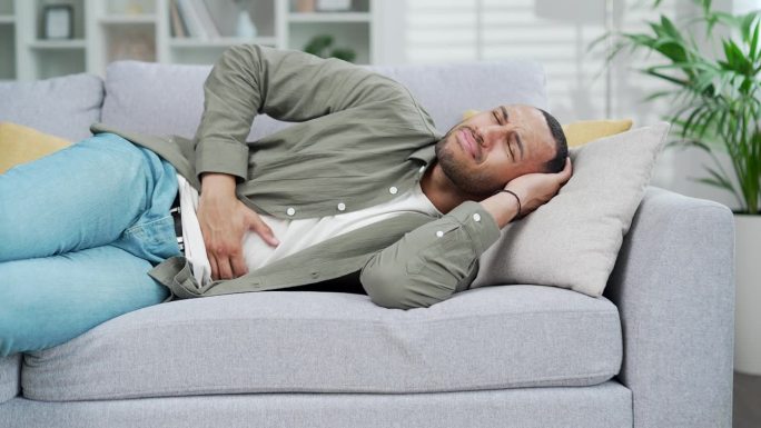 年轻的成年男子躺在沙发上突然感觉腹部胃痛，胃炎的问题。