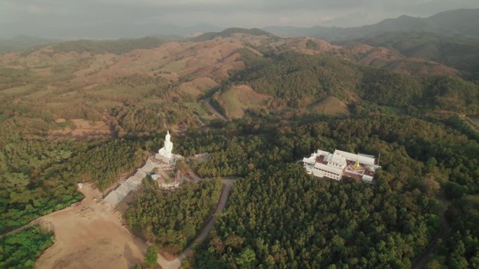 美丽的风景风景飞行视图，大白色佛像附近的佛教寺庙，金色的宝塔和白色的小教堂在高原上，周围有丰富的树木