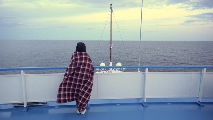 女孩站在船的甲板上，用毯子裹着，挡风