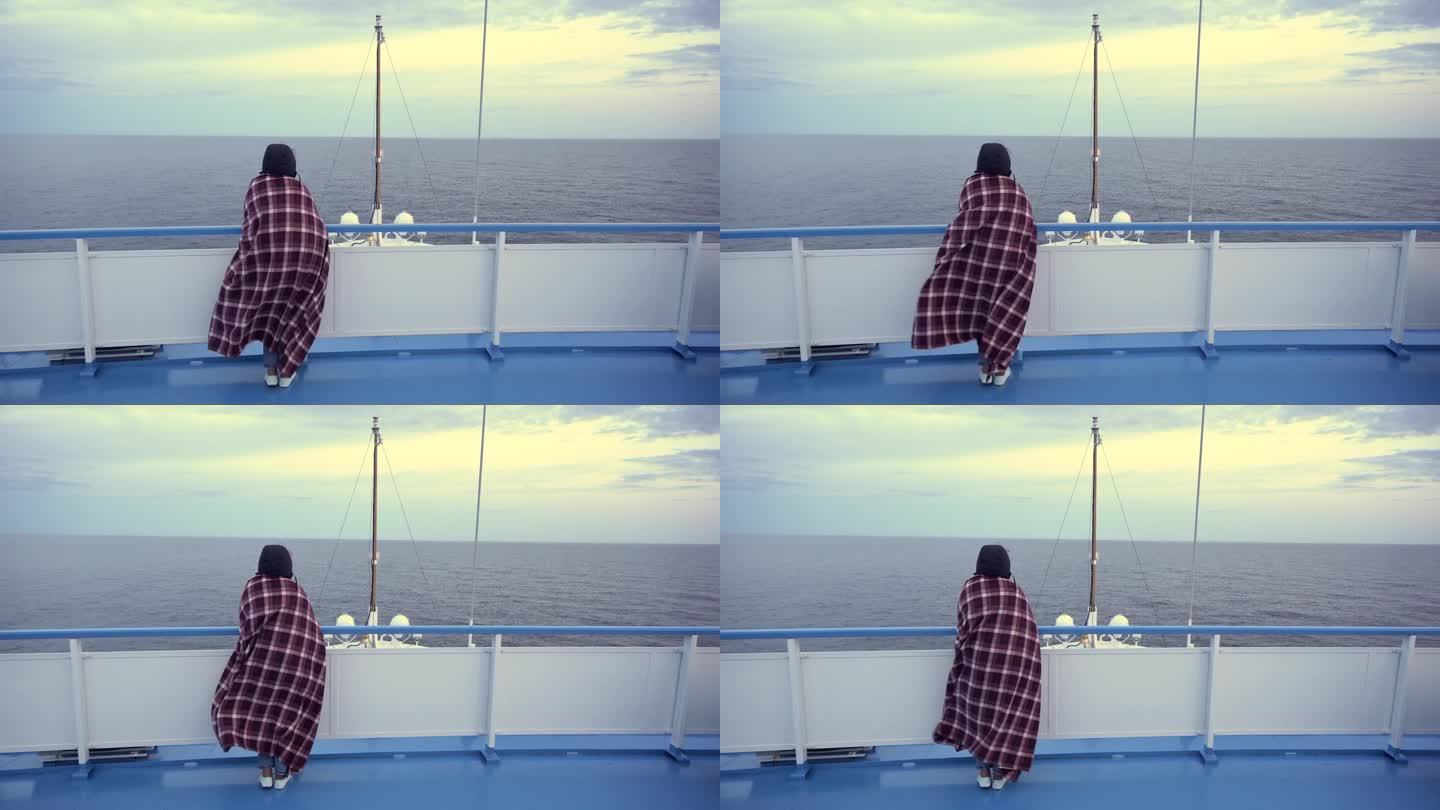 女孩站在船的甲板上，用毯子裹着，挡风