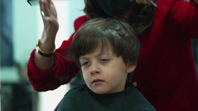 小孩在发廊理发的特写镜头。专业发型师为小男孩剪发梳理，神情严肃沉思