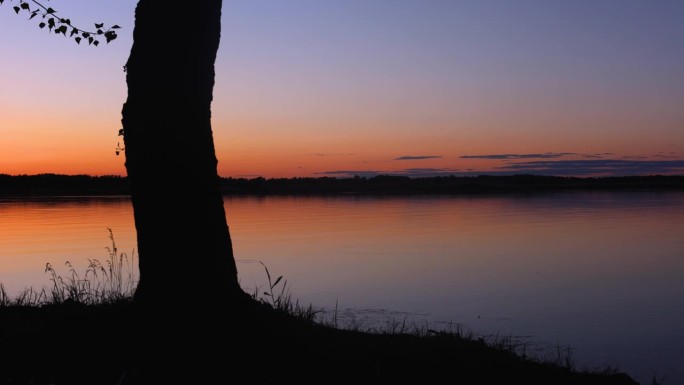 水泵旁美丽的夕阳和岸边的树随着时间流逝，渐渐暗下来。黄昏，晴朗的天空，水面，太阳落在河上。傍晚江景如