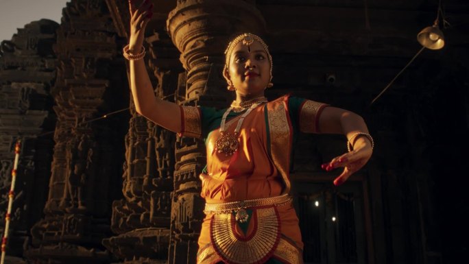 活泼的印度妇女穿着传统服装，用表情丰富的脸和迅速的动作跳舞的慢动作肖像。在古老的石庙欣赏南亚民间舞蹈