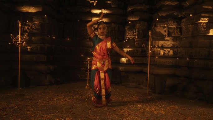 缩小镜头，印度妇女穿着传统服装，穿着五颜六色的纱丽，一边看着镜头，一边跳舞。富有表现力的年轻女性在庙