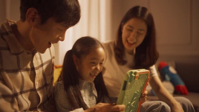 一个韩国家庭在家里用数码平板电脑共度时光的特写。年轻的父母在教育游戏中帮助他们的女儿解决问题。支持性