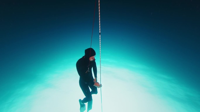 自由潜水员在绳子上锻炼。一名自由潜水者在开阔的海面上沿着绳索训练，然后潜到深海