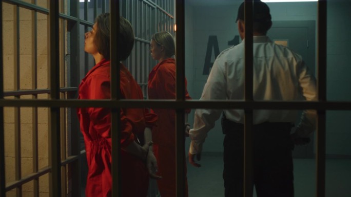 两名女囚犯站在牢房前的金属栅栏前