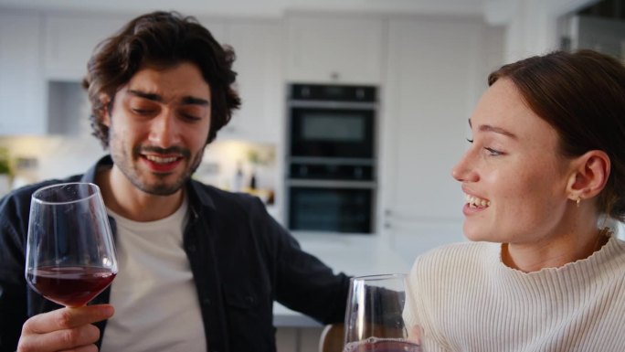 年轻夫妇在家里的厨房里喝着红酒，边说边笑