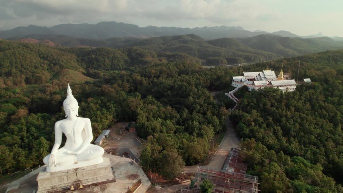 位于佛教寺院附近的佛像鸟瞰图，周围环绕着绿色的森林和山脉，是灵性和宁静的宗教旅行场所