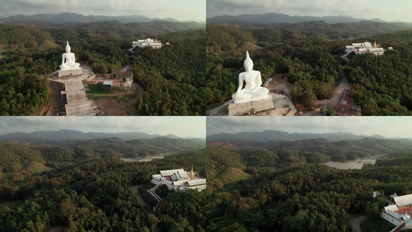 位于佛教寺院附近的佛像鸟瞰图，周围环绕着绿色的森林和山脉，是灵性和宁静的宗教旅行场所