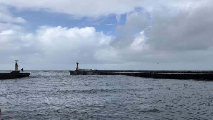 海浪冲击着港口防波堤的入口防护墙，防波堤边上的摄影师正在拍照