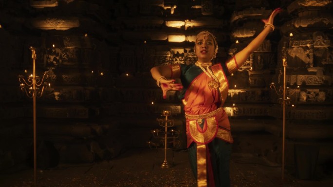 一位活跃的印度妇女的慢动作肖像，在烛光照亮的寺庙里从事传统民间舞蹈的迷人表演。一个迷人的和文化丰富的