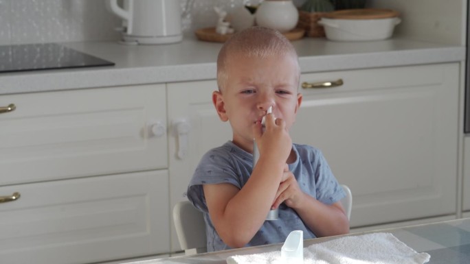 妈妈用吸鼻器和鼻喷雾器把生理盐水喷在她蹒跚学步的孩子的鼻子里，小男孩很冷，还流鼻涕