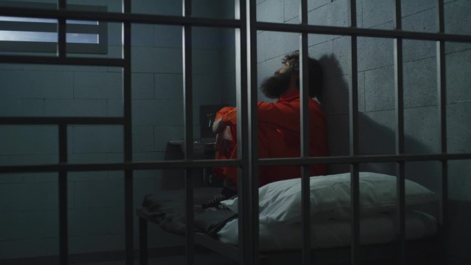 穿橙色制服的囚犯坐在牢房的床上