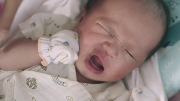 一个刚醒来的亚洲新生儿的脸部特写。大声地哭，因为他饿了。