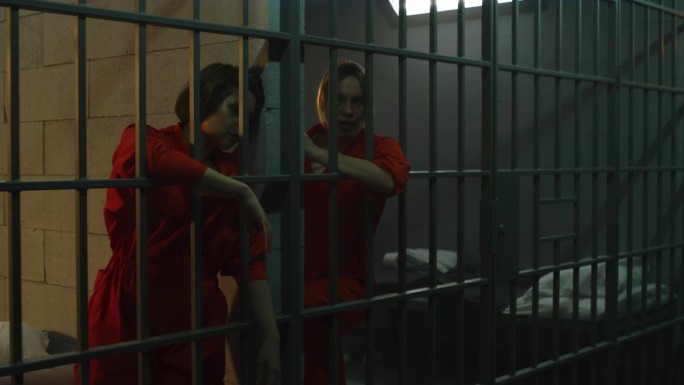 女囚犯站在监狱牢房的金属栅栏后面，互相击掌