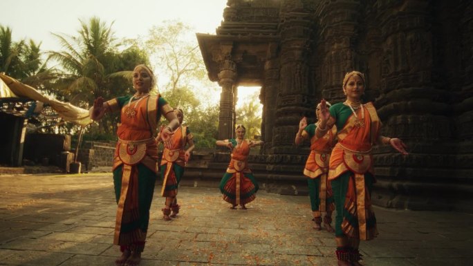 穿着传统服装的印度妇女看着镜头，穿着五颜六色的纱丽跳着Bharatanatyam。年轻女性分享民间舞