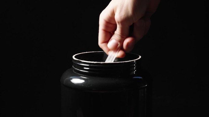 一个黑色的大罐子，我拿出一个量勺装满蛋白粉，孤立的黑色背景，放大效果。