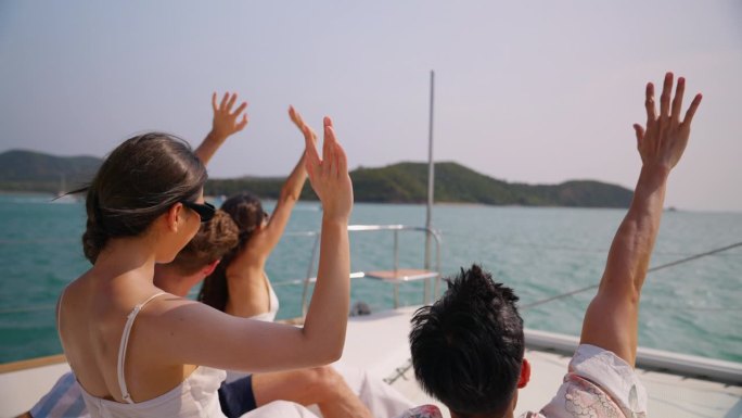 一群不同的朋友一起坐在游艇甲板上。迷人的年轻男女聚在一起，庆祝节日，双体船在夏日夕阳下航行。