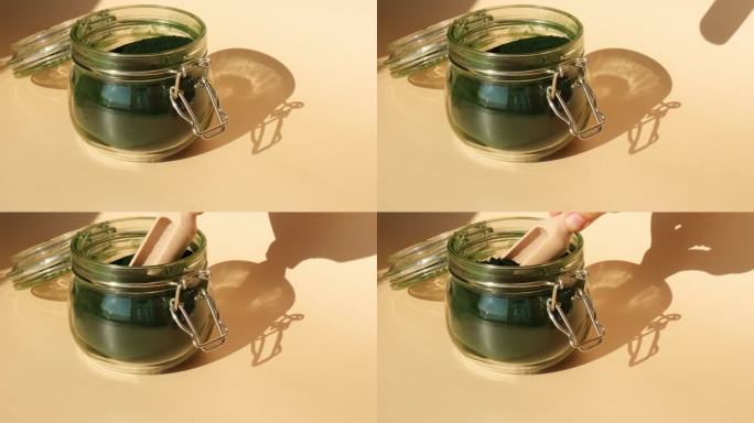 有机蓝绿藻螺旋藻粉食品，用木勺装于玻璃罐中。小球藻对健康的益处。维生素和矿物质。排毒膳食补充剂海藻超