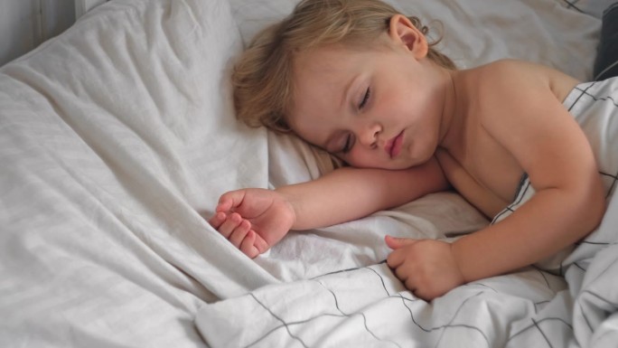 安静可爱的宝宝睡在家里的床上。熟睡的小孩。两岁的女孩安静地睡在家里的房间里。宁静的梦。可爱的脸特写。