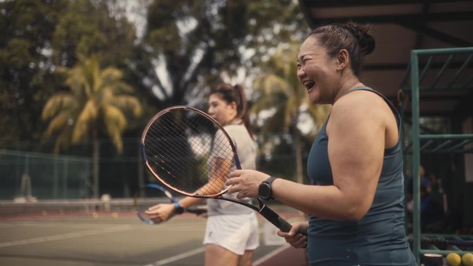 2名站在网球场旁兴奋地看着教练学习的亚洲中国女网球学生