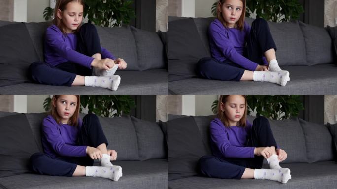 一个可爱的金发小女孩把带星星的白袜子穿在脚上。孩子的独立性。低龄学童着装技巧的发展。