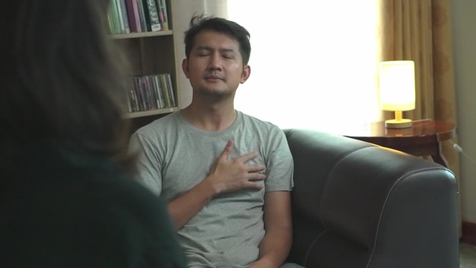 一位亚洲年轻人在和他的女心理医生谈话时看起来若有所思。